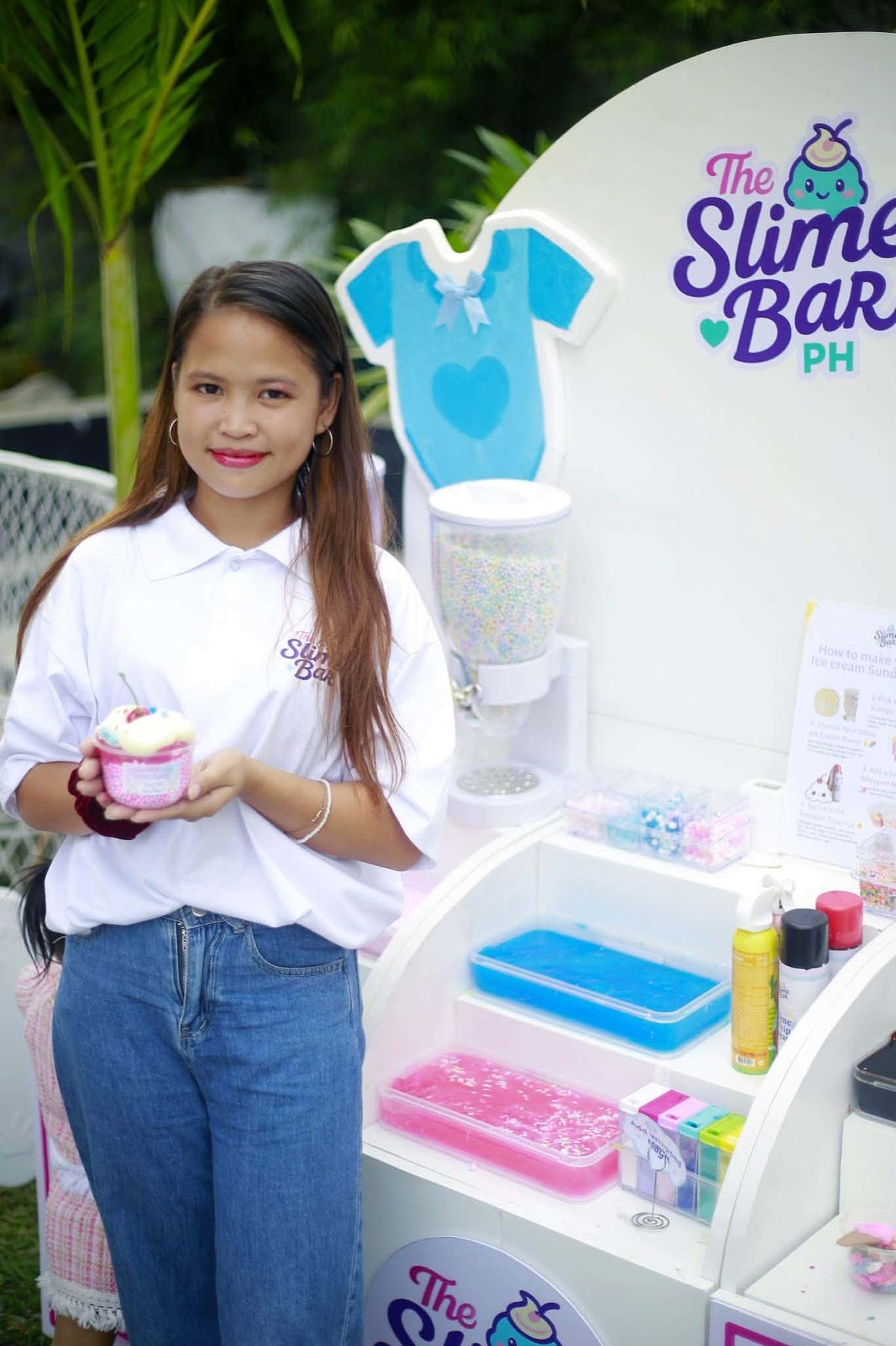A staff member holds a cup of pink slime beside The Slime Bar PH counter